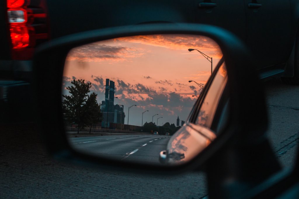 An image of a car's side-view mirror reflecting the road and peach sunset behind the car.

Photo by Hunter James on Unsplash