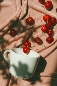 A top-down photo of a collection of cherries on a tan/peach blanket, spilling from sea foam mug. 

Photo by Olesia Misty on Unsplash