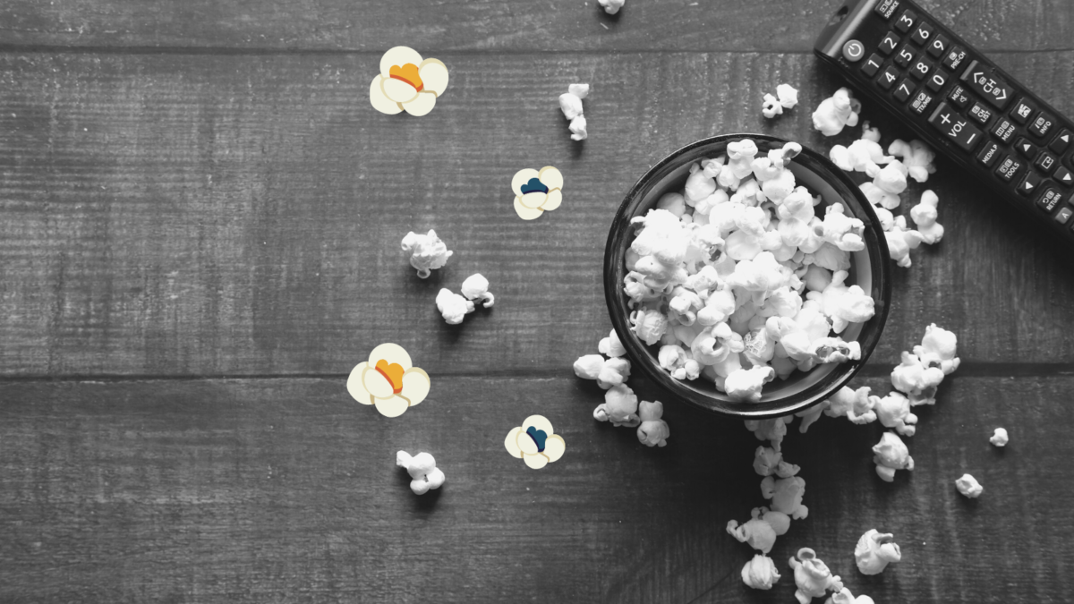 Popcorn spilling out of a bowl. A TV remote is on the table next to the bowl.