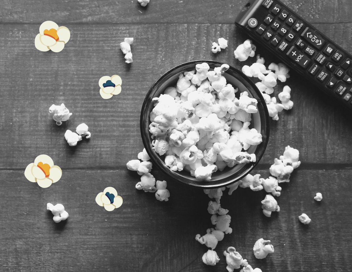 Popcorn spilling out of a bowl. A TV remote is on the table next to the bowl.