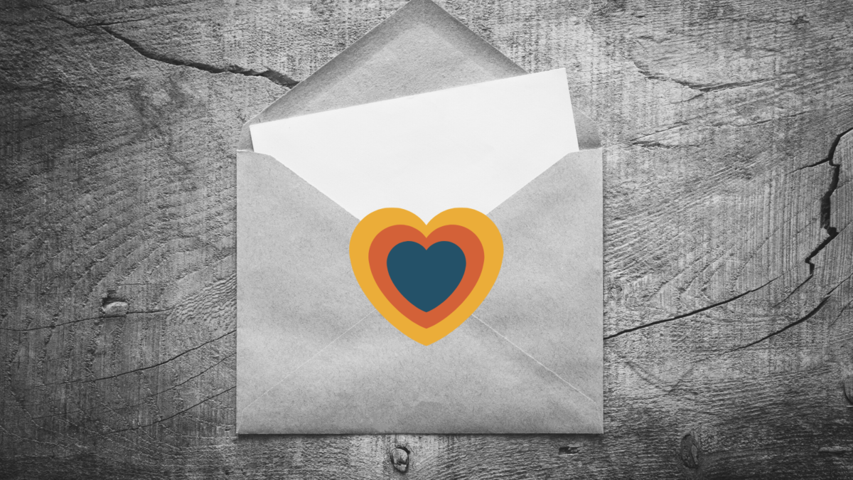 An open envelope on a table. A piece of blank paper sticks out. A multi-colored heart (blue, yellow, orange) is in the middle of the envelope