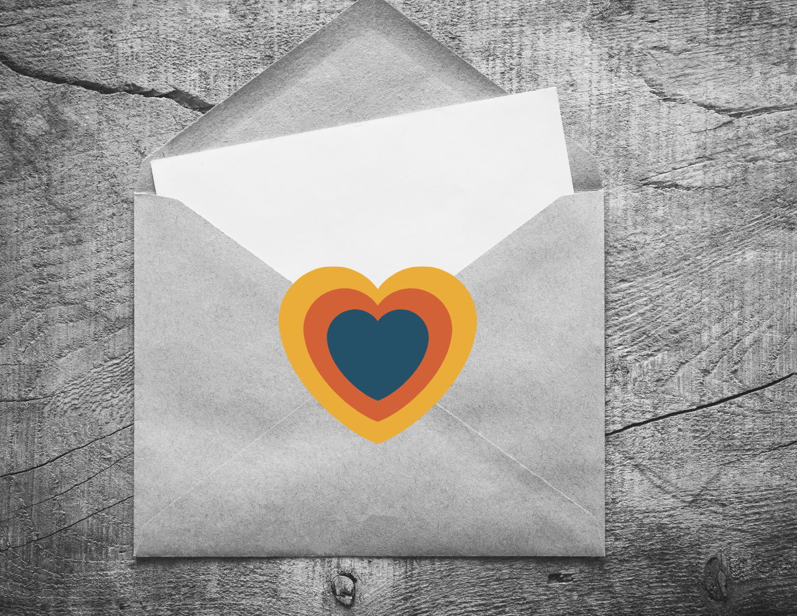 An open envelope on a table. A piece of blank paper sticks out. A multi-colored heart (blue, yellow, orange) is in the middle of the envelope