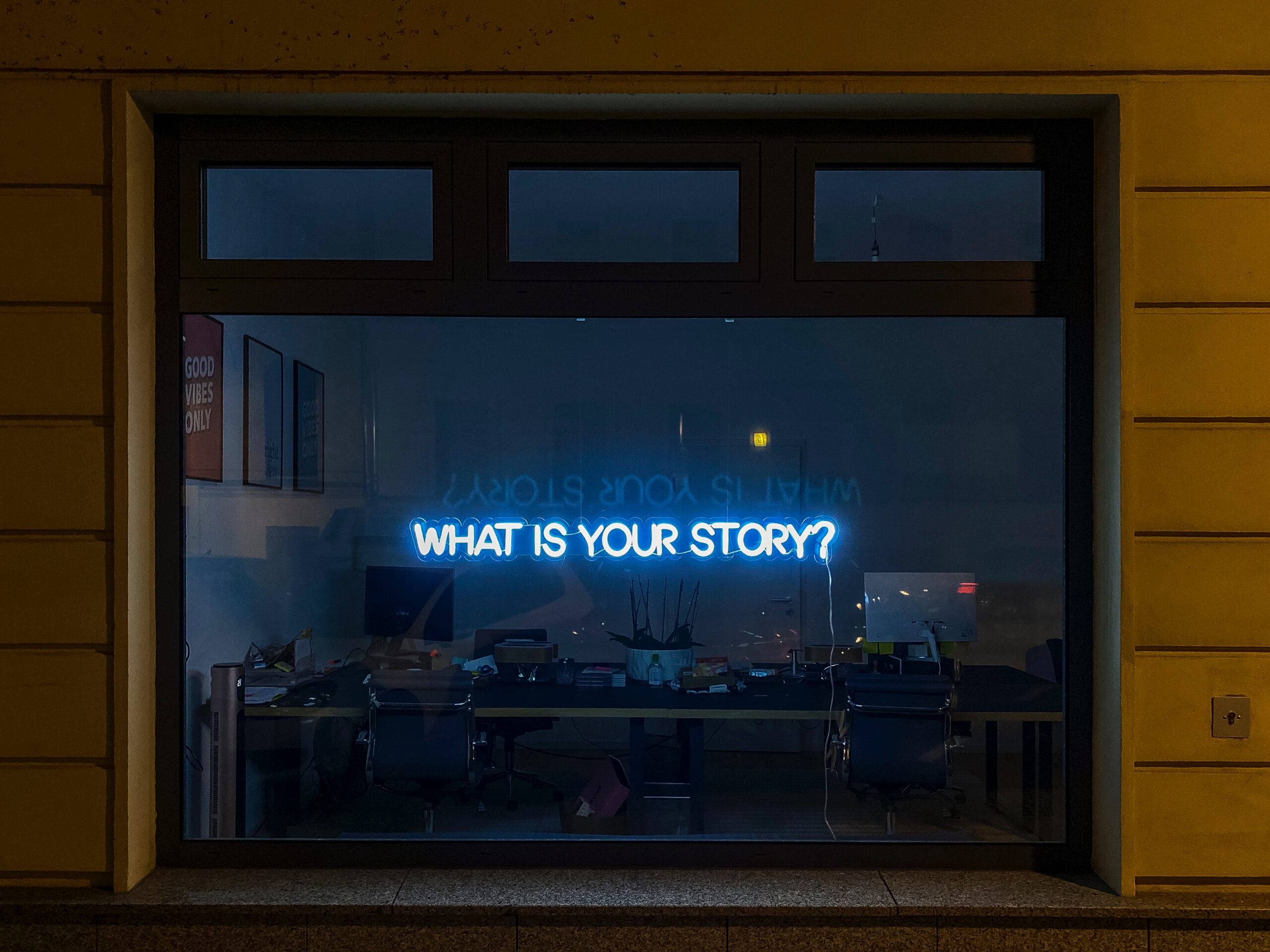 In the window of a store, there is a blue holographic light sign that reads "What's your story?"
